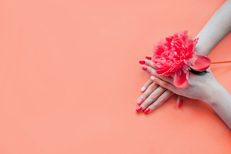 Coral color creative bright trendy summer manicure with nails of different color. female hands with art nail design on pink background and fuchsia peony flower.
