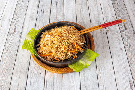 Stir-fried curly chinese noodles with fried vegetables and chicken hole metal bowl and with chopsticks on white table