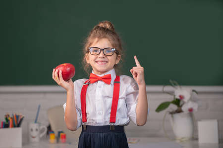 Portrait d'une étudiante écolière nerd tenant une pomme avec une expression surprenante pointant du doigt contre le tableau noir. premier jour à l'école.