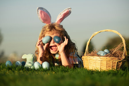 Mignon garçon enfant lapin excité avec des oreilles de lapin. enfant avec des oeufs de pâques dans le panier en plein air. garçon portant sur l'herbe dans le parc. chasse aux oeufs de pâques. portrait d'enfants fynny. Banque d'images