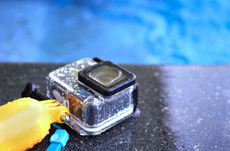 Action camera in waterproof case and floater grip on poolside and blur swimming pool