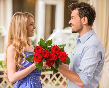 Happy young couple with roses bouquet on a date.
