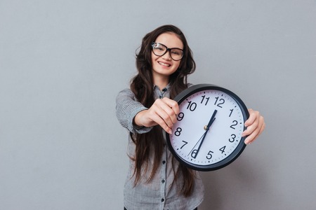 smiling cute asian woman in glasses and gray shirt holding clock