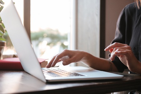 Cropped image of young woman sitting at the table in cafe and using laptop computer Stock Photo