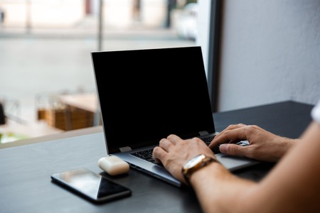 Cropped image of young business man using laptop computer while sitting by the table in cafe