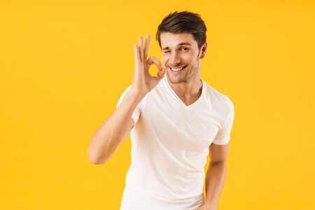 Photo of happy man in basic t-shirt smiling at camera while showing ok sign isolated over yellow background Stock Photo