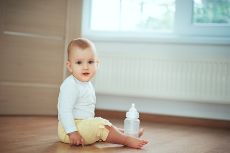 愛らしい小さな赤ちゃんは ミルクや水のボトルと床の上の寝室に座って 笑っています 幼児の子供の子供の人々の概念 子供のライフスタイルと居心地の良い家 の写真素材 画像素材 Image