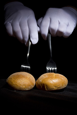 Buns on the forks and hands in white gloves on a black background