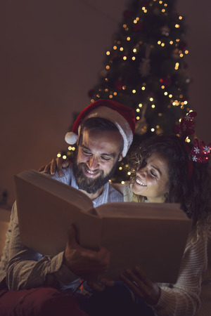 Couple in love enjoying winter holidays at home, looking an old photo album on Christmas night - 107805983