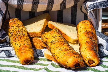 Sausages baked in dough sprinkled with salt and poppy seeds in a rustic composition. sausages rolls, delicious homemade pastries.
