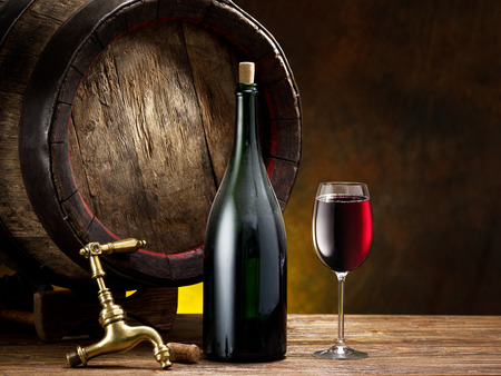 Still life con un bicchiere di vino, bottiglie e botte sul tavolo ... Botte tavolo con vetro