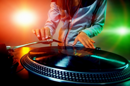 Dj hands on equipment deck and mixer with vinyl record at party