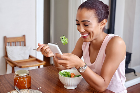 Heureuse jeune femme appréciant un saladier sain avec un téléphone portable à la maison cuisine