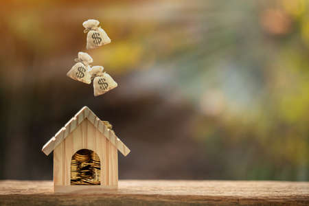 Modèle de maison et pièce d'or et sac d'argent déposé sur le dessus mis sur le bois dans le parc public, économiser de l'argent pour acheter une maison ou un prêt pour l'investissement commercial du concept immobilier.
