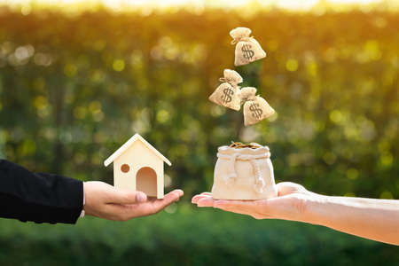 Main d'homme d'affaires et de femme tenant une maison modèle et un sac d'argent se présentant dans le parc public, économiser de l'argent pour acheter une nouvelle maison ou un prêt pour planifier l'investissement commercial du concept immobilier.