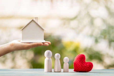 Main de femme tenant le modèle de maison pour sélectionner ou donner à la famille en bois et au coeur rouge sur bokeh dans le parc public, l'achat d'une nouvelle maison ou d'un bien immobilier en cadeau au concept de l'être aimé. Banque d'images
