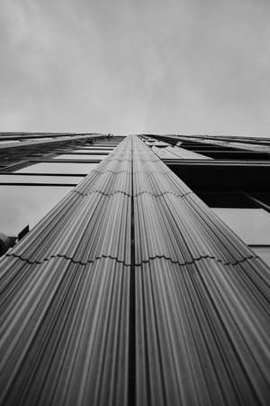 A low angle greyscale of a modern skyscraper under the cloudy sky Banco de Imagens