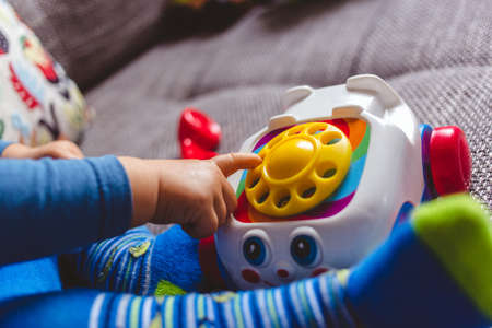 A cute baby in blue tights playing with a toy telephone on the coach