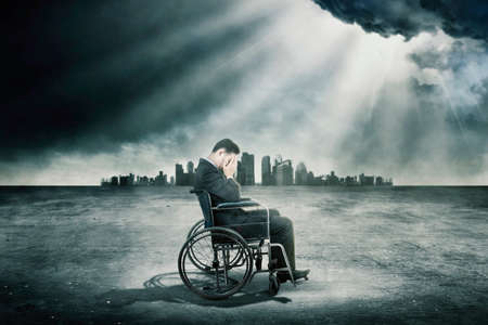 Disabled businessman feeling sad while sitting on the wheelchair under sunlight with cityscape background
