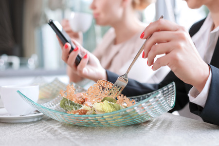 Schließen Sie herauf Foto von den Händen auf einer Frau, die eine Gabel isst einen Salat und einen Handy hält, der einige wichtige E-Mail, in einem Restaurant während des selektiven Fokus des Business-Mittagessens liest Foto auf Lager