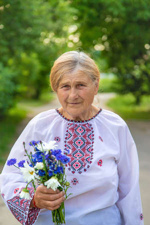 An Old Ukrainian Woman In An Embroidered Shirt With A Bouquet Of Flowers. Selective Focus.