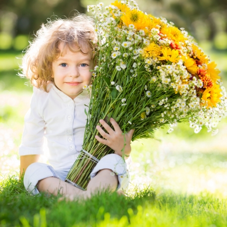 Happy child with bunch of flowers sitting on green grass in spring park Фото со стока