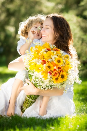 Happy child and woman with bouquet of spring flowers sitting on green grass. Mother`s day concept