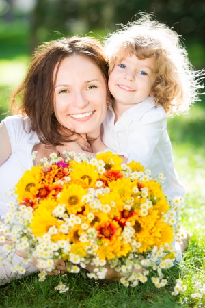 Happy child and woman with bouquet of spring flowers lying on green grass. Mother`s day concept