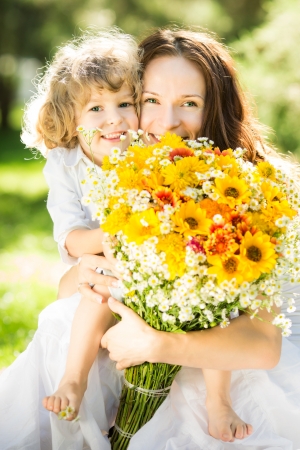 Happy family with big bouquet of spring flowers having fun outdoors against blurred green background. Mothers day celebration concept Фото со стока