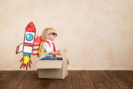 Happy child playing with toy rocket at home. funny kid driving cardboard box indoor. success and win concept