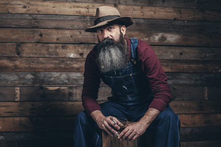 vintage worker man with long gray beard in jeans dungarees holding