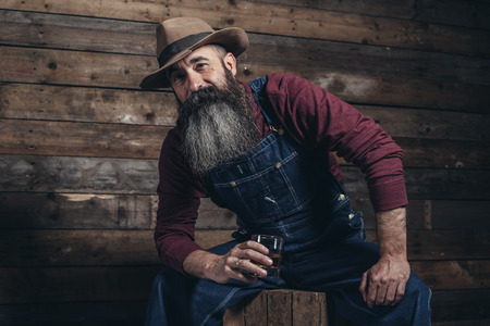 vintage worker man with long gray beard in jeans dungarees holding