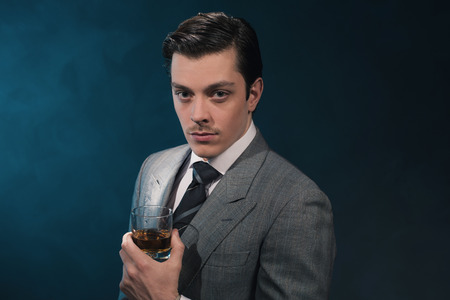 ヴィンテージ 1940 年代ファッション男スーツとネクタイの青い壁にウィスキーのグラスを保持しています の写真素材 画像素材 Image