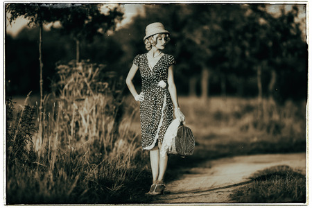 1930 年代の古典的な黒と白の写真の夏農村風景の中 ドレスのファッション女性とハンドバッグ麦わら帽子立っています 肩越しに見ています の写真素材 画像素材 Image