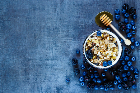 Granola dans la tasse vintage, baies foncées et miel pour le petit déjeuner délicieux sur fond grunge avec un espace pour le texte sur la gauche, vue de dessus. Photo en stock