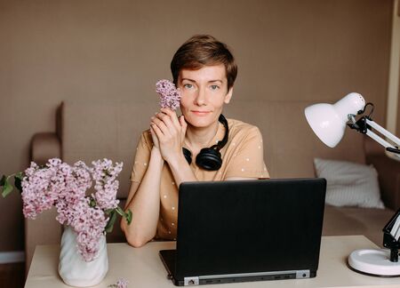 Holiday Woman With Lilac Flowers In A Bright Home Office Working With A Laptop