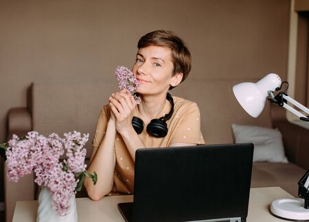 Holiday Woman With Lilac Flowers In A Bright Home Office Working With A Laptop