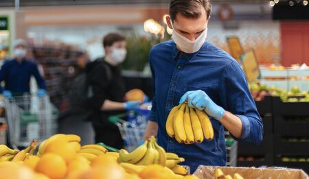 Man in protective gloves choosing bananas in a supermarket.
