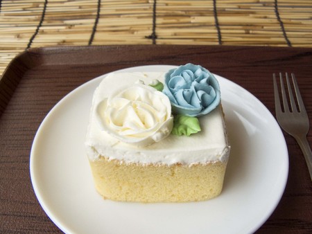 シフォン雪フラワー ケーキの側面図を閉じます バニラのシフォン ケーキ クリーム青と白のケーキの上に花の飾られています 白プレート 木製のテーブル背景に フォークを置きます の写真素材 画像素材 Image