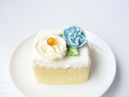 シフォン雪フラワー ケーキの側面図を閉じます バニラのシフォン ケーキは クリーム色の花とオレンジ ゼリー ボールで飾られました 白い皿とフォークを置きます 白い背景上に分離 の写真素材 画像素材 Image