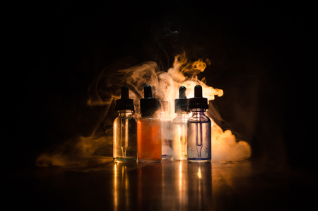 Conceito Vape. Nuvens De Fumo E Garrafas Líquidas Do Vape No Fundo Escuro. Efeitos De Luz. Útil Como Fundo Ou Vape Propaganda Ou Fundo Vape. Fotos, Retratos, Imágenes Y Fotografía De Archivo