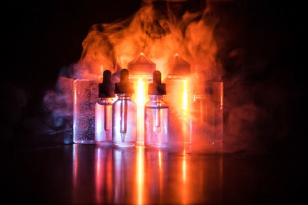 Vape concept. smoke clouds and vape liquid bottles on dark background. light effects. selective focus