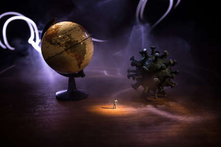 Corona virus global pandemic concept. miniature man standing near big corona virus novel in dark. creative decoration with fog and backlight. selective focus