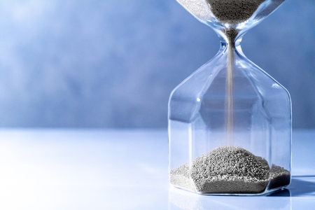 Sliver Sand Running Through The Shape Of Modern Hourglass On White Table.time Passing And Running Out Of Time. Urgency Countdown Timer For Business Deadline Concept