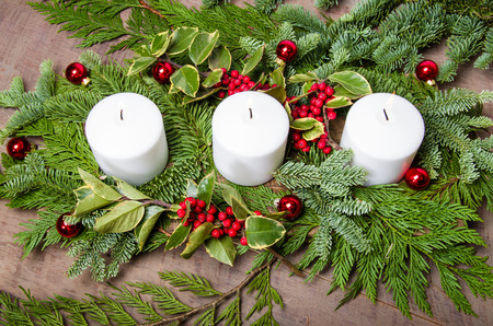 An evergreen Christmas centerpiece with three white candles and variegated holly - 34163353