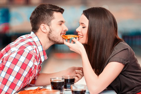 Nahaufnahmebild der jungen attraktiven Frau und des Mannes, die ein Stück Pizza mit Bowlingbahn im Hintergrund isst