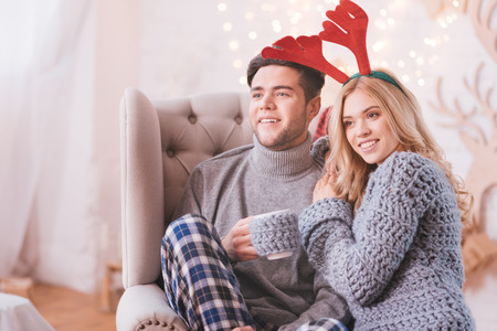Joyful moments. Delighted nice loving couple smiling and looking in front of them while sitting together in the armchair