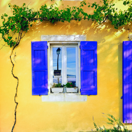 Open window with lavender color wooden shutters on an ocher color plastered wall on a sunny day. Bonnieux village, Provence, France Фото со стока