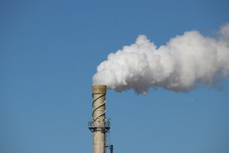 Steam comes out a chimney above a factory with white steam cloud on clear blue sky in rotterdam
